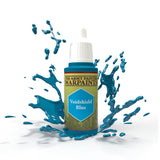 A small paint bottle with a white cap and a green label stands amid splashes of glossy blue paint. The label reads “THE ARMY PAINTER WARPAINTS” and “Voidshield Blue.”