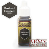 A small paint bottle with a white dropper cap and a dark olive-and-gold label reading “THE ARMY PAINTER WARPAINTS” and “Hardened Carapace.” A dark hexagon beside it reads “Hardened Carapace WP1430.”